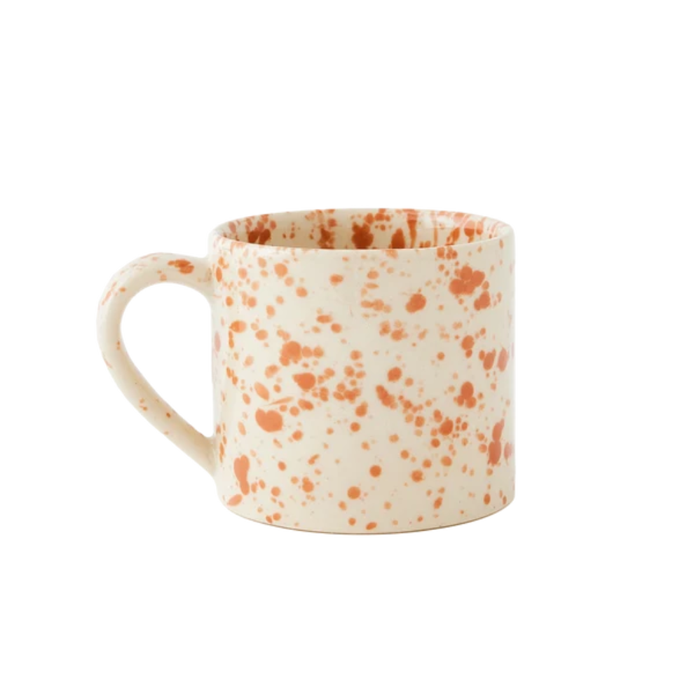 A straight-sided round mug with a warm cream base and translucent burnt orange splattered pattern, shown against a plain white background.