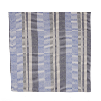 A square woven textile napkin with a striped pattern in shades of cobalt blue, navy blue, gray, and off-white, shown flat against a solid white background.