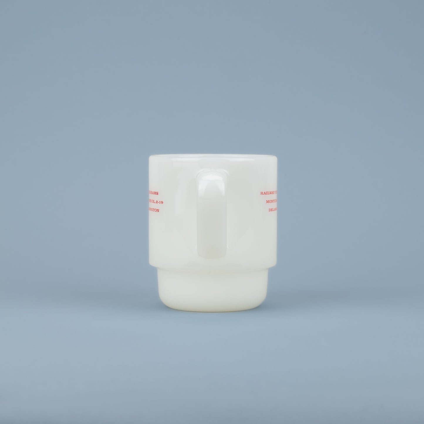 Handle of a white milk glass mug with red lettering on the sides against a blue background