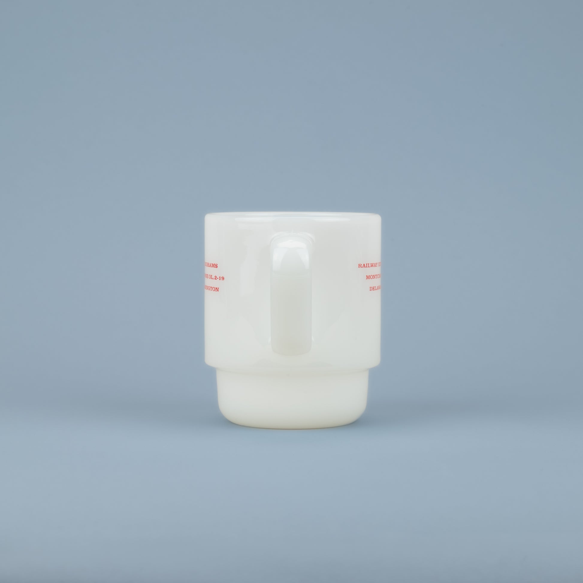 Handle of a white milk glass mug with red lettering on the sides against a blue background