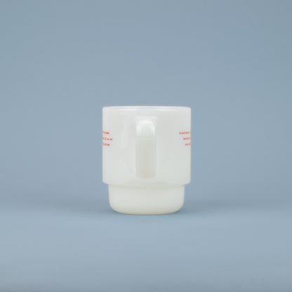 Handle of a white milk glass mug with red lettering on the sides against a blue background
